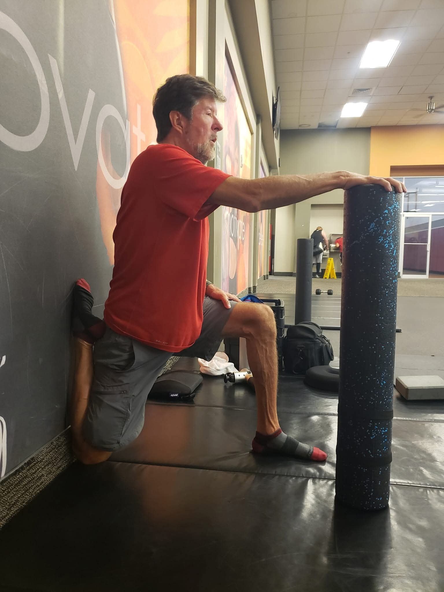 John Kilgore kneeling in a supported quadriceps stretch with one foot against a wall