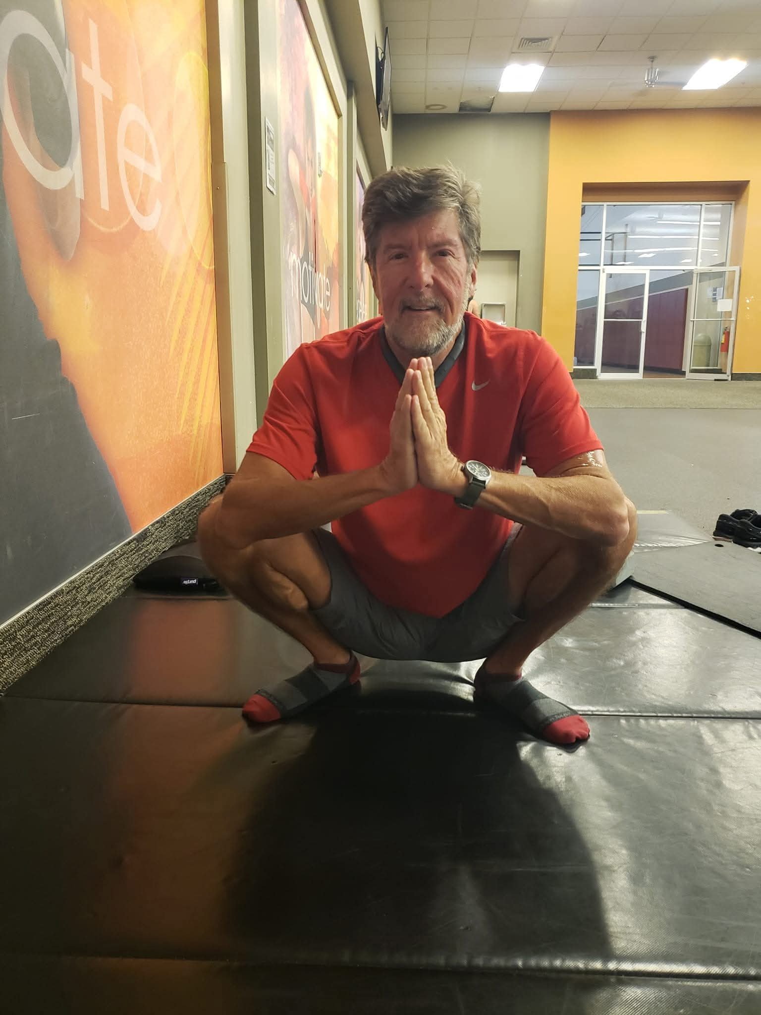 John Kilgore holding a deep squat stretch with palms pressed together